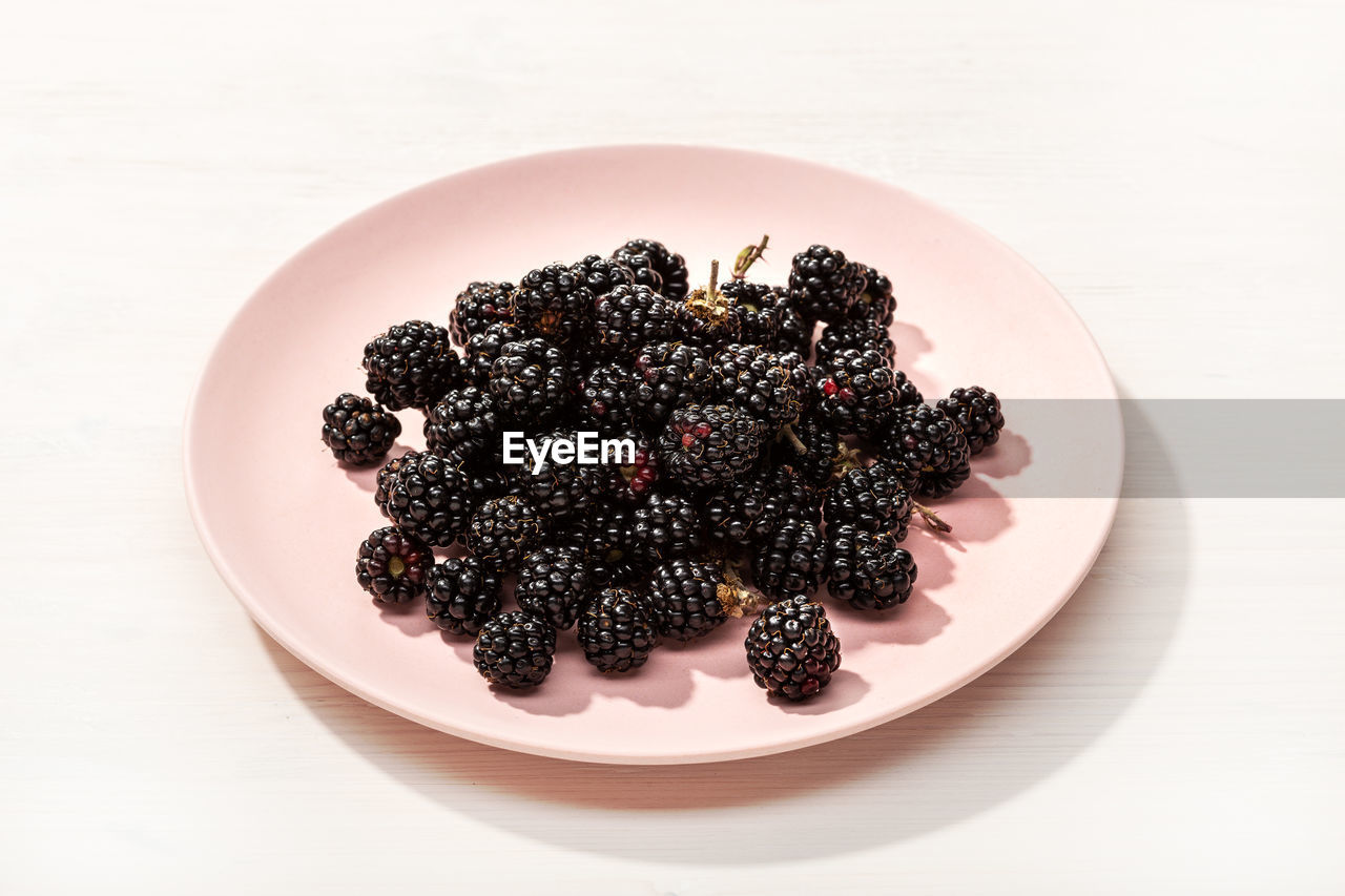 Fresh wild blackberries in plate on white wooden background. edible wild fruit