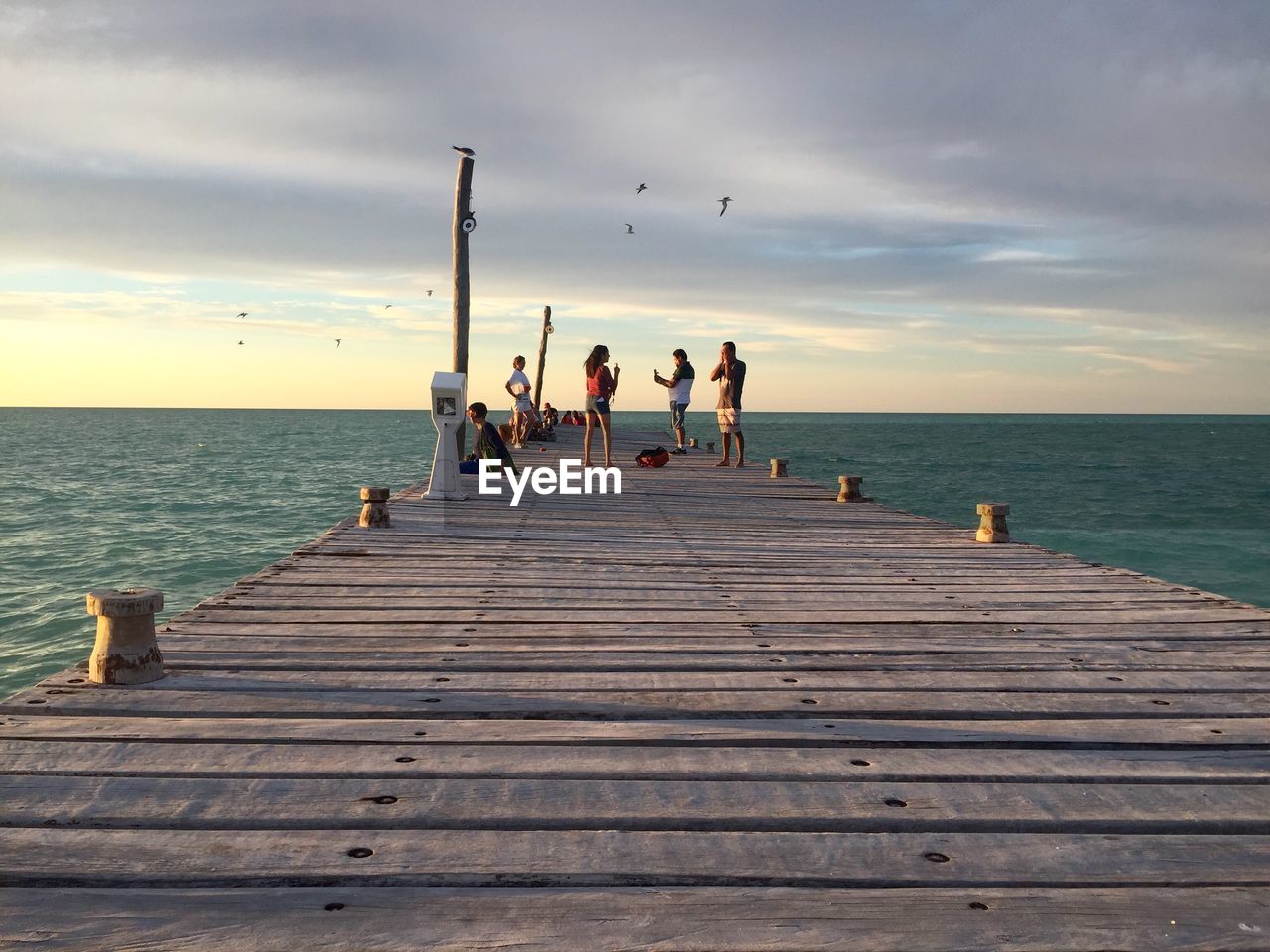 People standing on pier over sea against cloudy sky