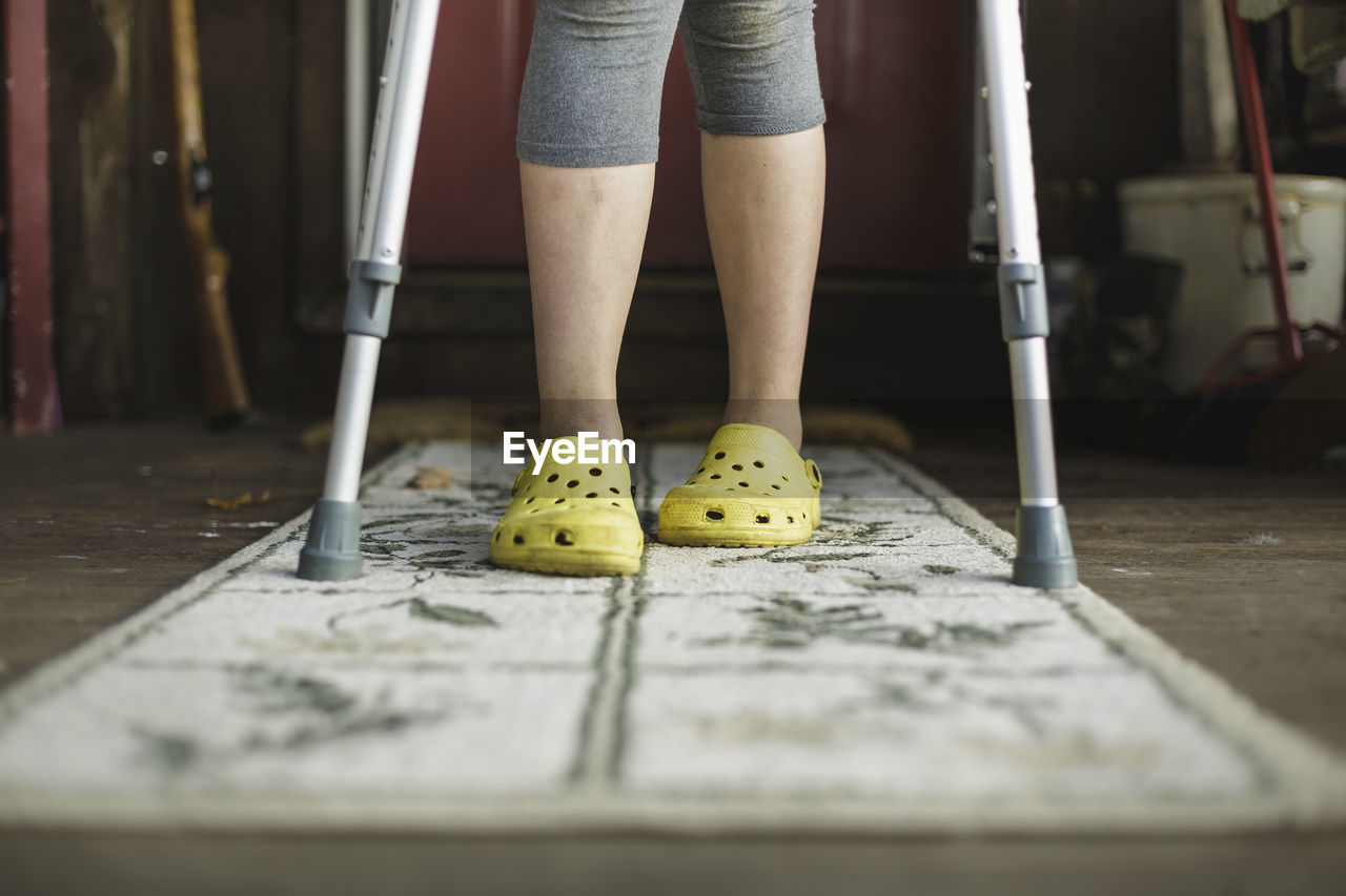 Low section of girl with crutches standing on rug at home