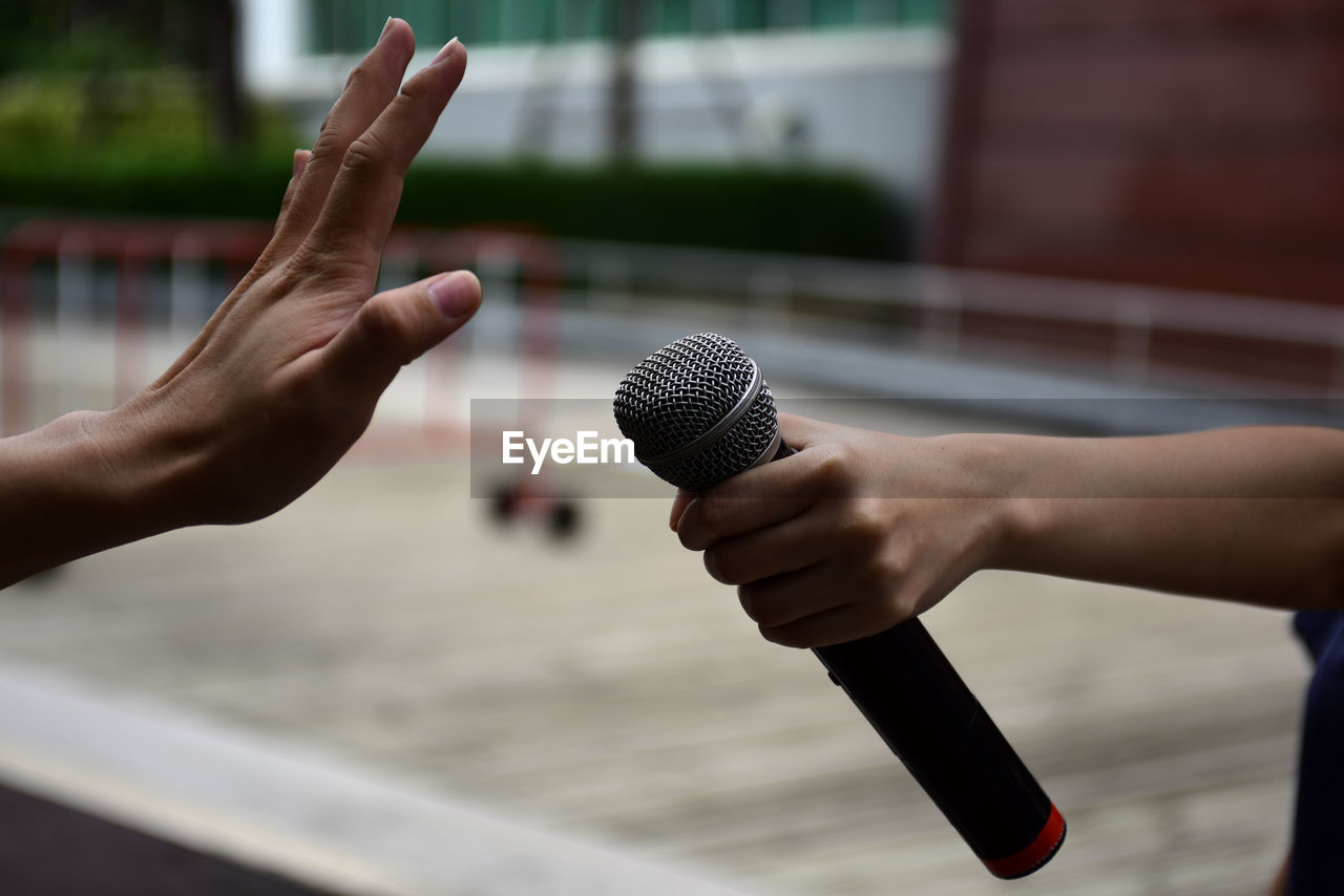 Cropped hand of woman holding microphone by man showing stop gesture