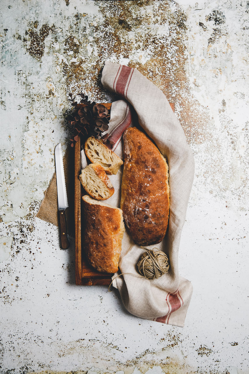 From above rustic composition with aromatic bread loaves on board with linen towel and knife on shabby surface