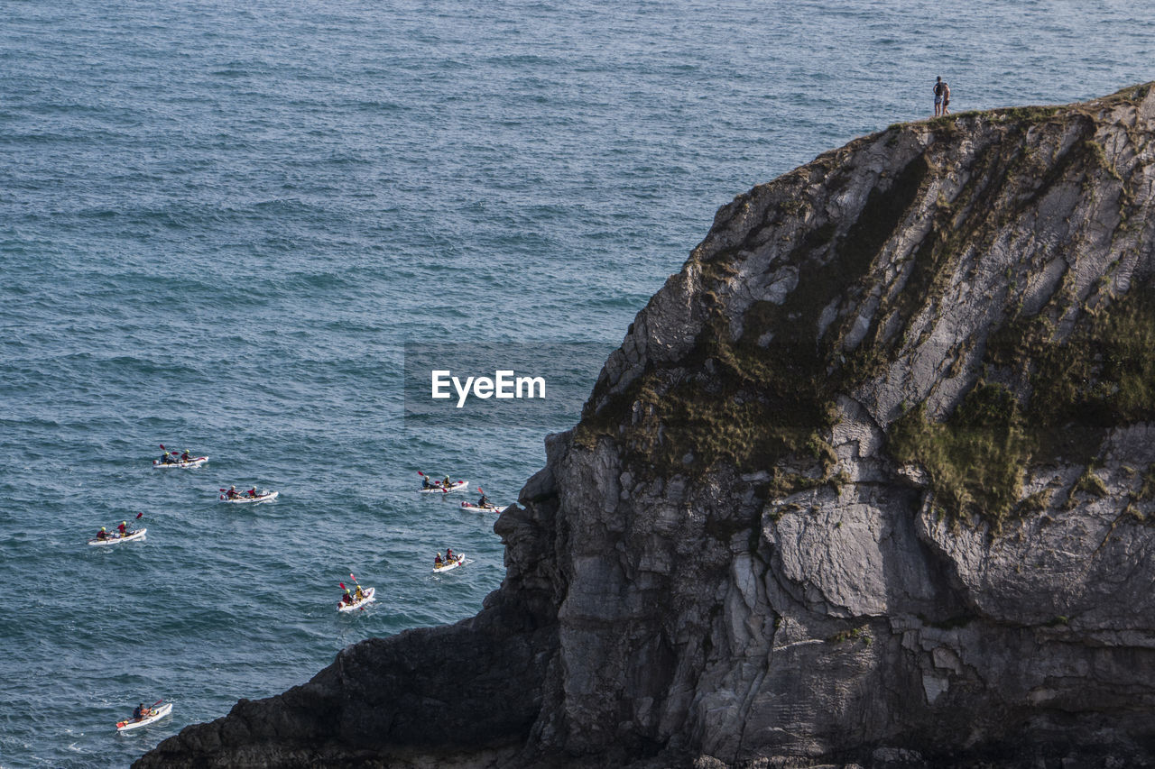 People on cliff looking at boat race in sea
