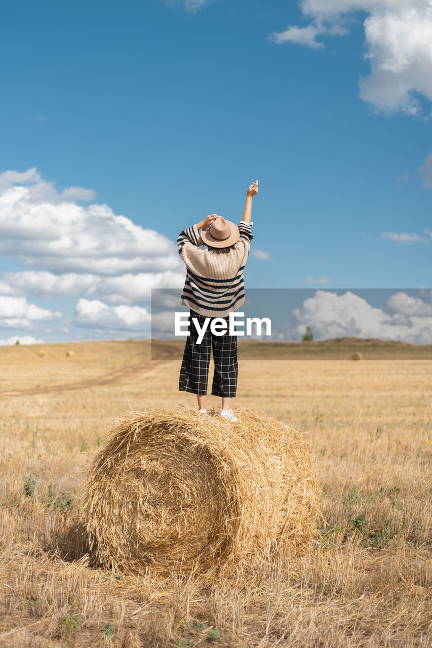 MAN STANDING BY HAY BALES ON FIELD