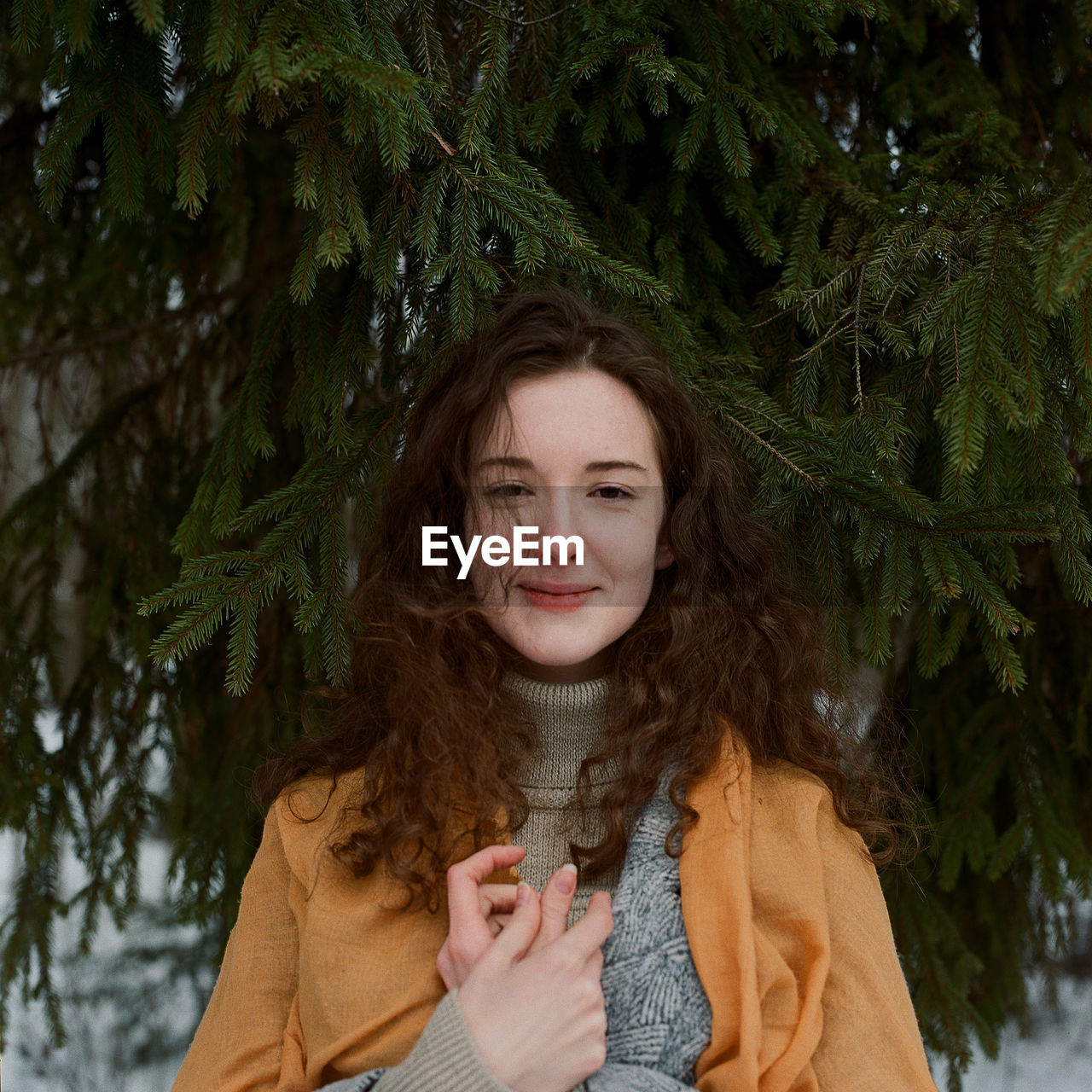 A woman stands on the shore of a frozen lake in a yellow scarf