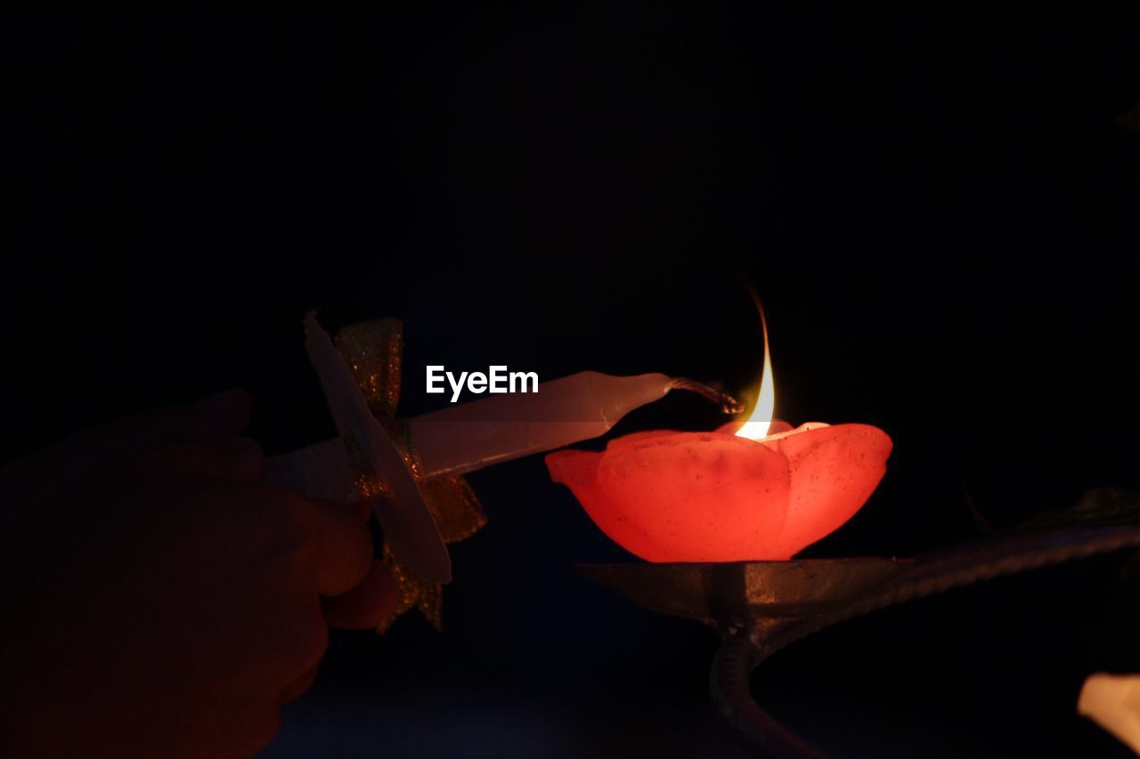 CLOSE-UP OF HAND HOLDING ILLUMINATED CANDLE