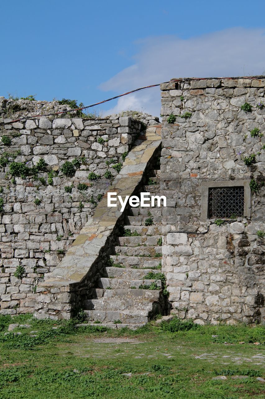 architecture, wall, ruins, built structure, history, ancient history, sky, stone wall, the past, building exterior, archaeological site, nature, no people, fortification, ancient, wall - building feature, building, rock, stone material, old ruin, day, old, grass, plant, outdoors, travel destinations, land, village, travel, clear sky, terrain, rural area, house, abandoned