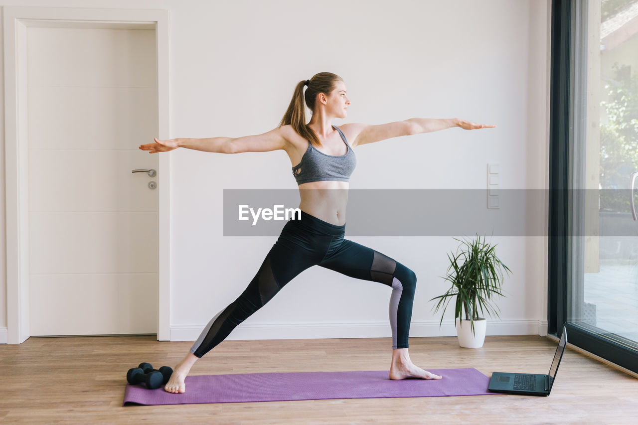 Young woman practices yoga class at home. the girl athlete stands in the pose of a warrior. 