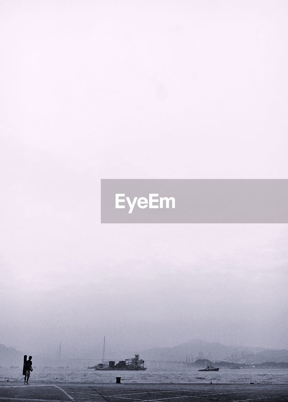 Man standing on pier by sea against sky