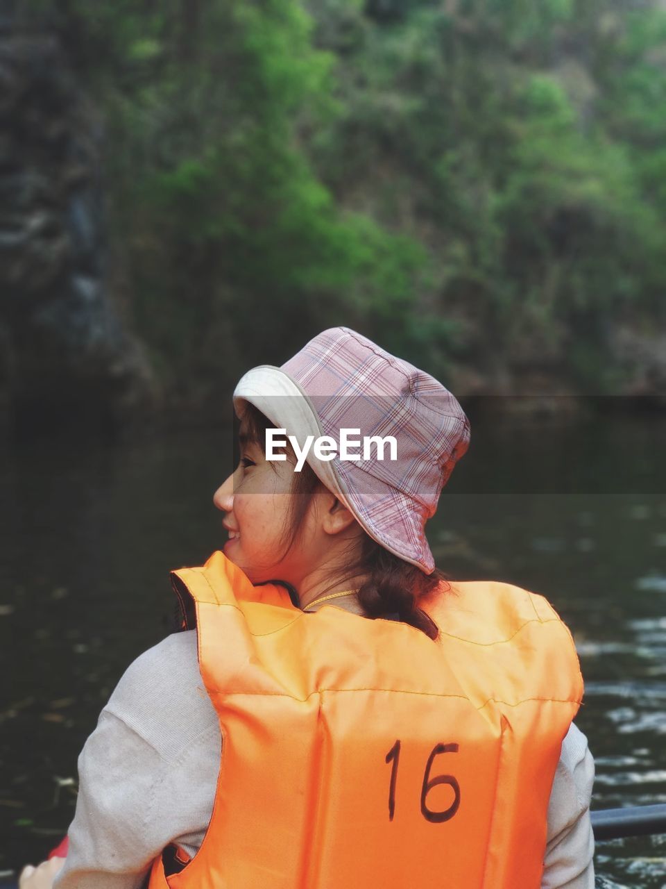 Rear view of woman with life jacket in river against trees