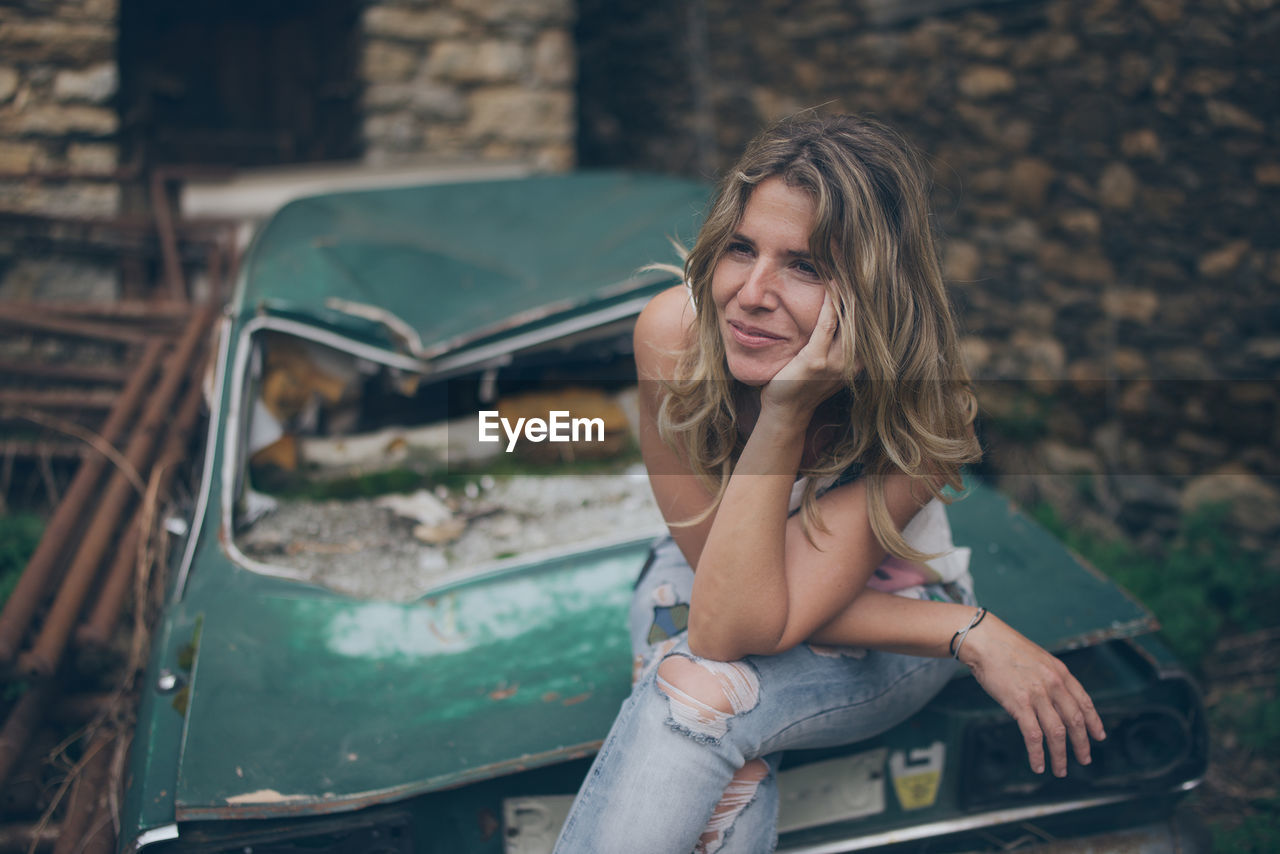 Young woman looking away while sitting on abandoned car
