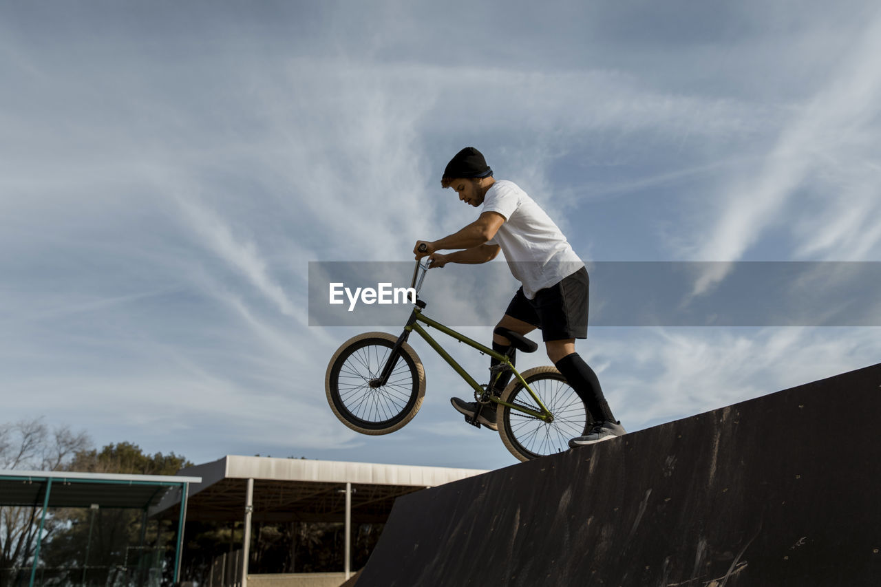 Bmx bike artist riding on ramp against sky during sunny day