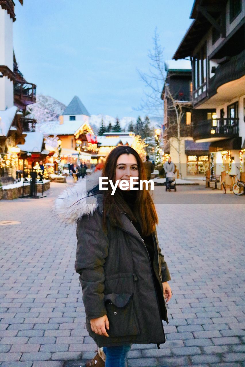 Portrait of smiling woman standing on street in city during winter