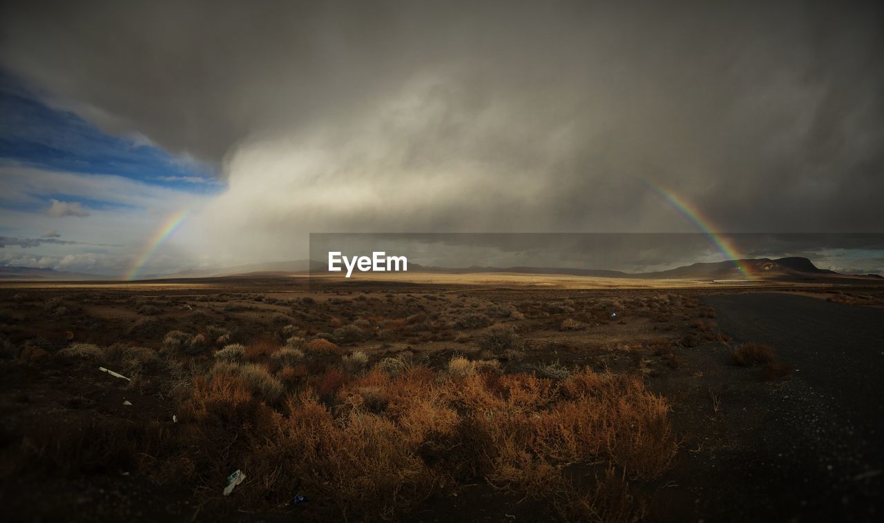 Scenic view of rainbow over field against cloudy sky