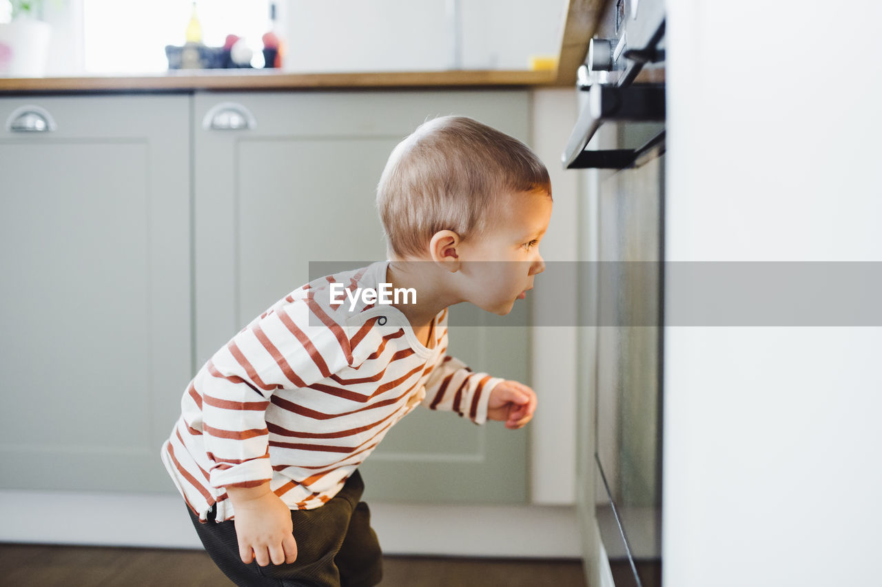 Toddler boy looking at oven in kitchen at home