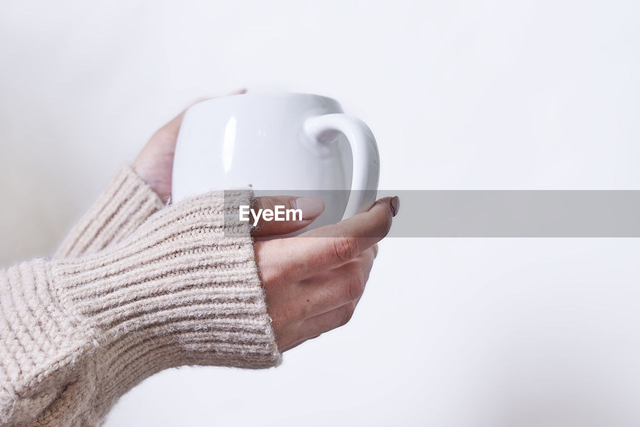 Female hand holding hot tea cup against white background. a woman in warm knitted sweater holds in
