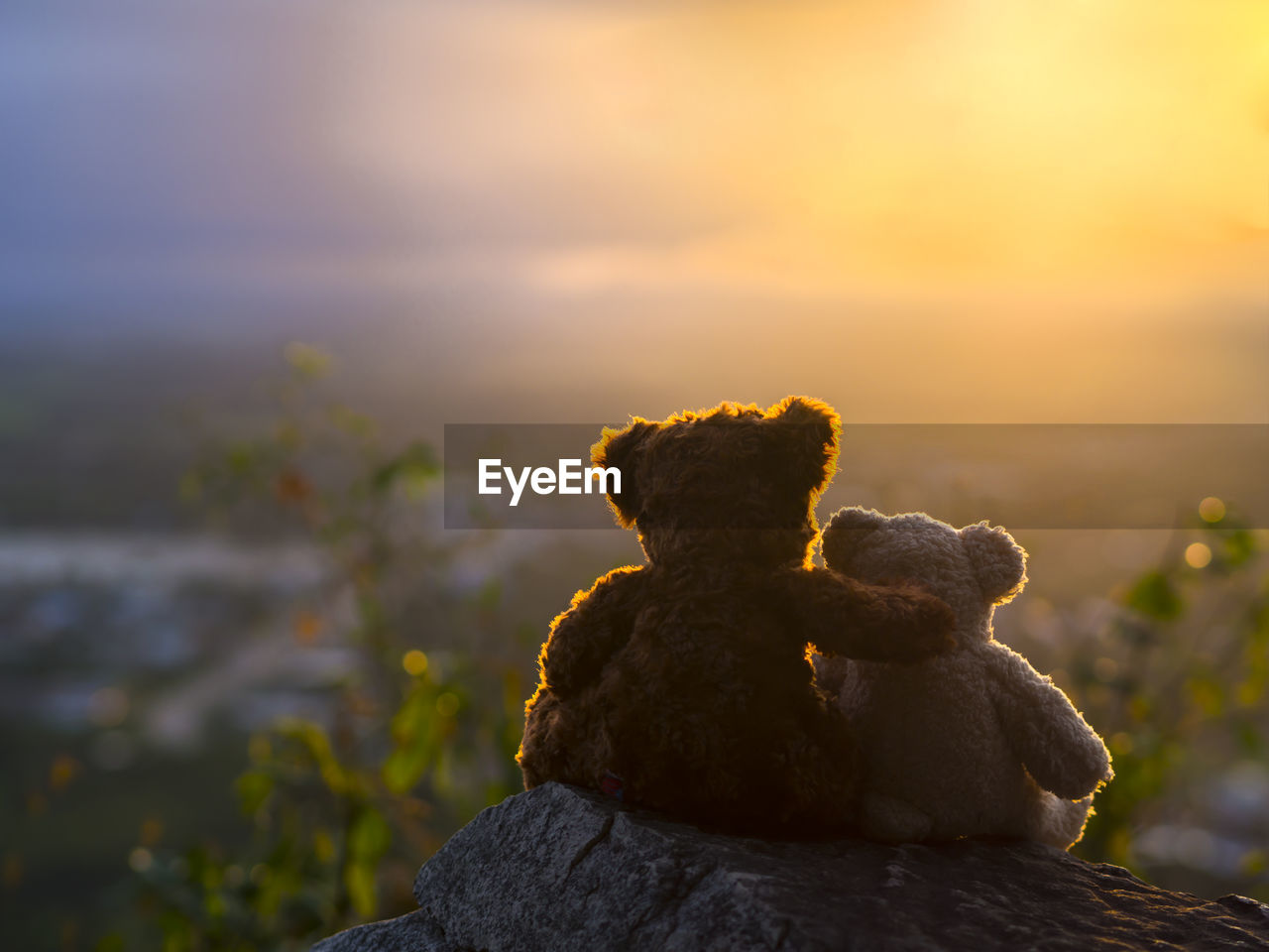 Stuffed teddy bears on rock against sky during sunset