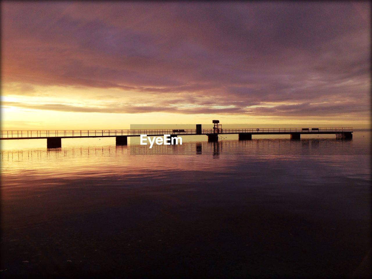 Pier over sea against cloudy sky during sunset