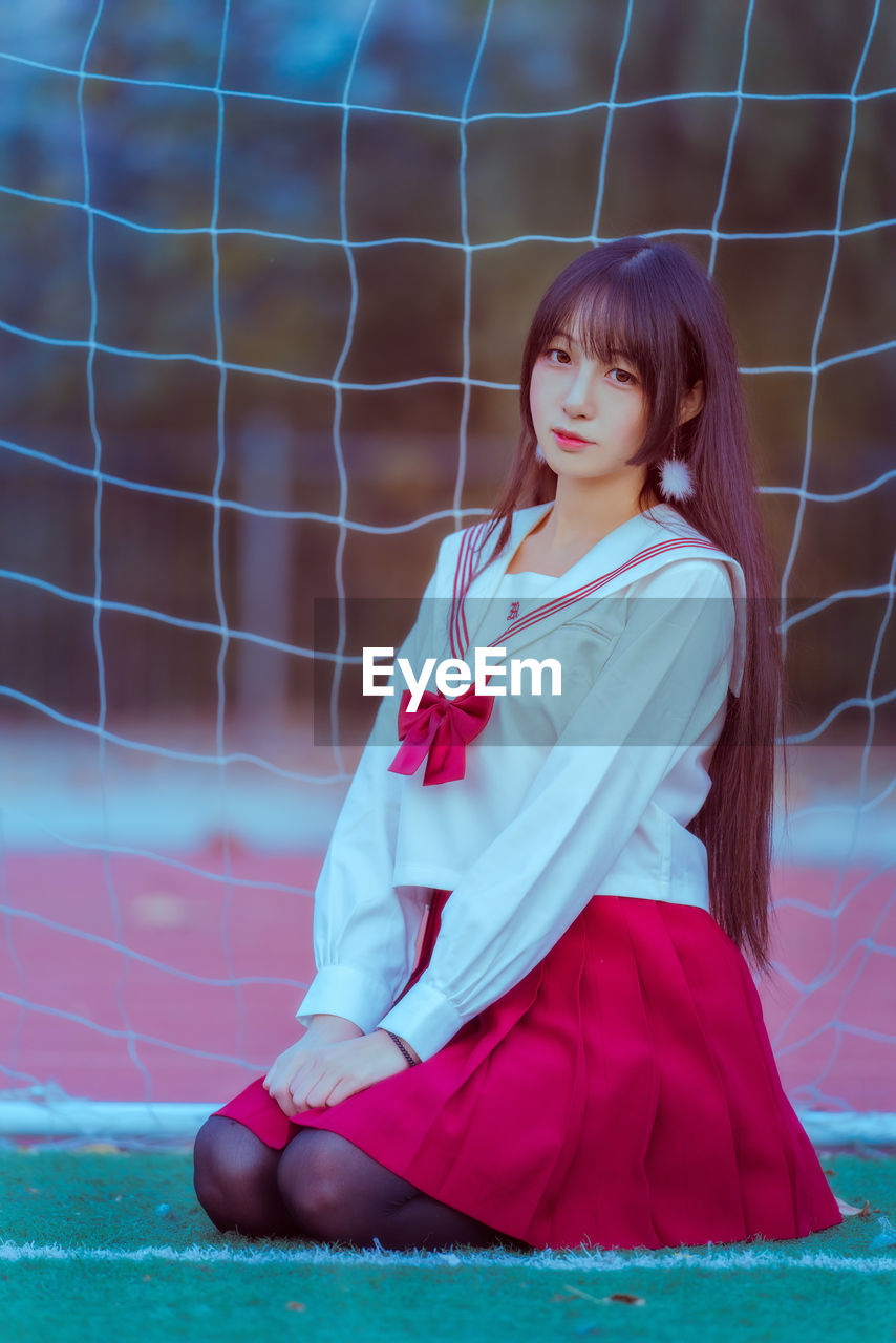 Portrait young woman sitting against net on soccer field