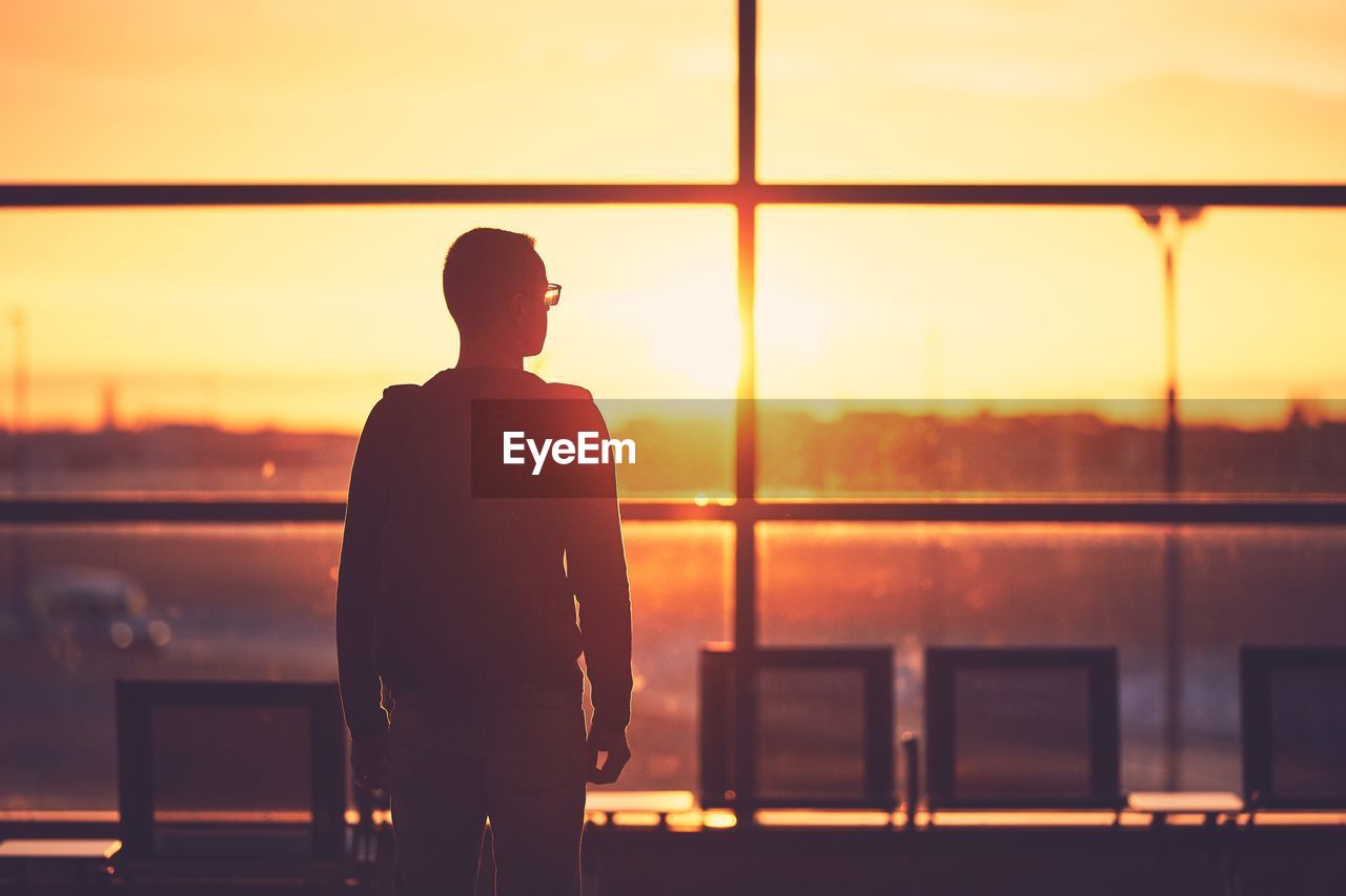 Rear view of man standing at airport during sunset