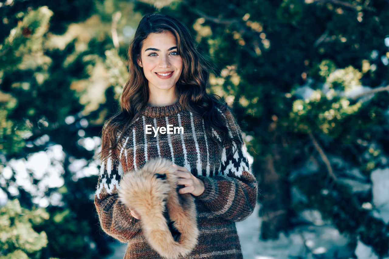 Portrait of smiling young woman against trees