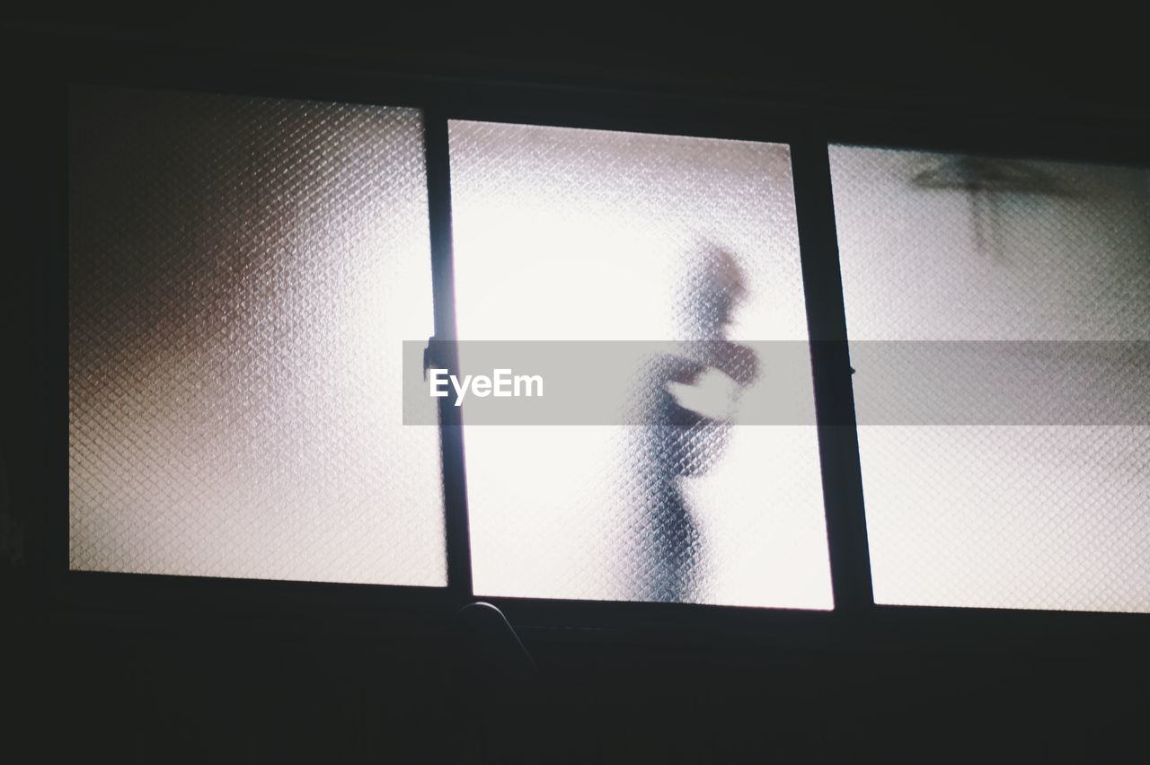 Low angle view of person shadow on frosted glass window