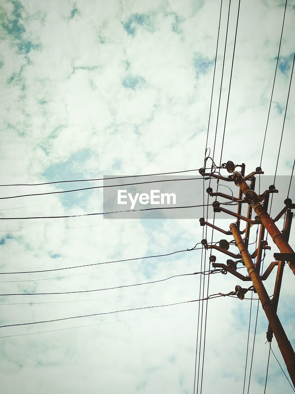 Low angle view of electricity pylon against cloudy sky