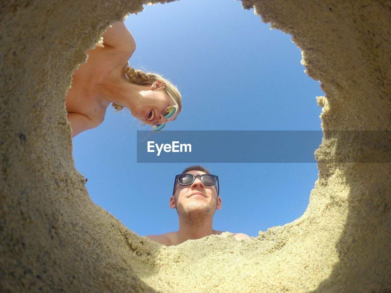 Shirtless man and woman seen through sand against sky