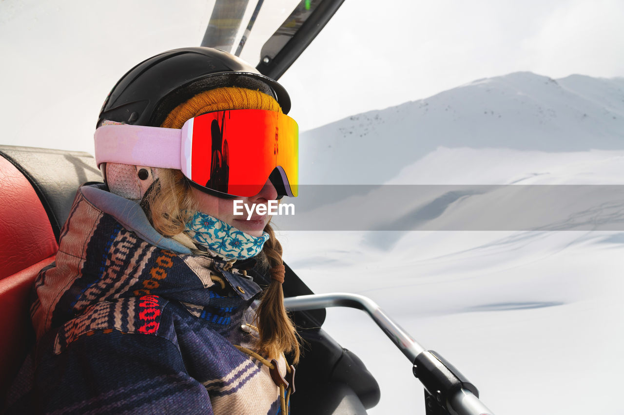 Portrait of a professionally dressed female skier in profile sitting in an open cabin of a ski lift