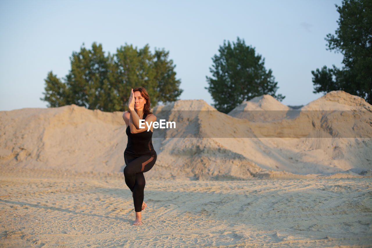 Confident mature woman practicing yoga on land during sunrise