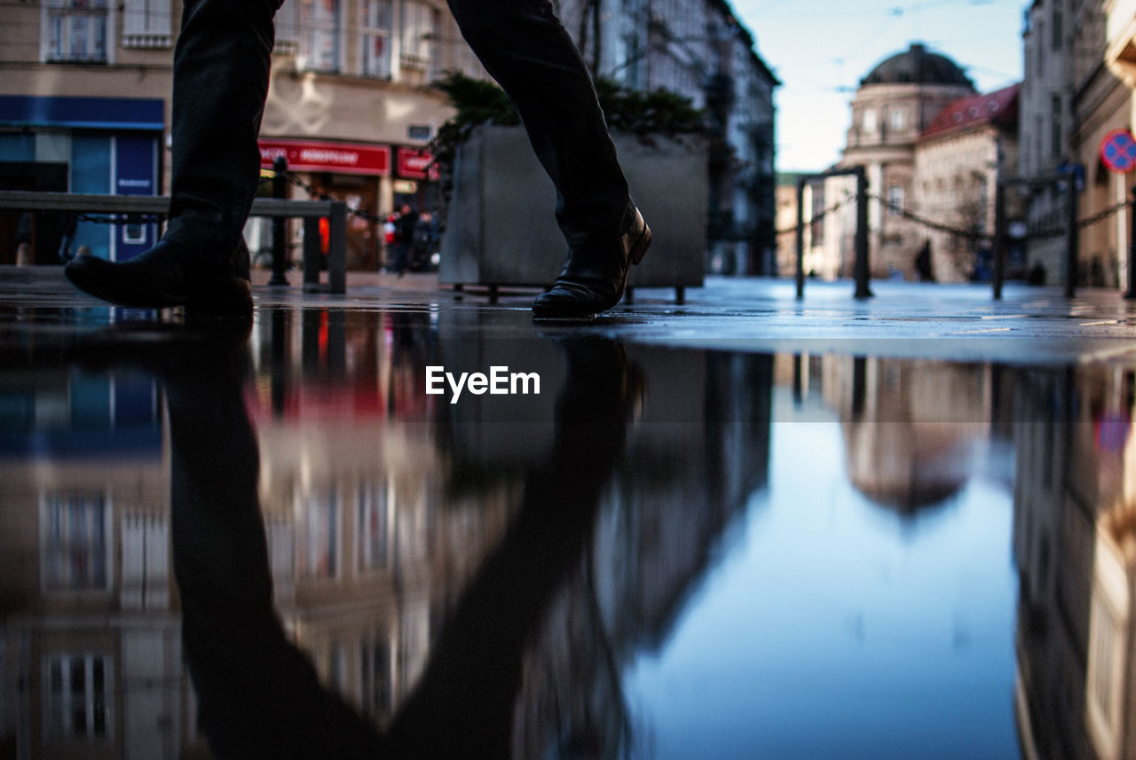 Low section of man walking on wet street in city during monsoon