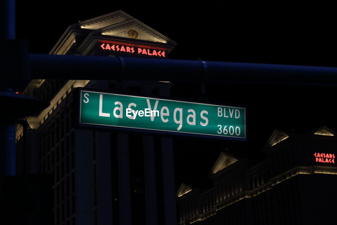 LOW ANGLE VIEW OF ROAD SIGN AGAINST ILLUMINATED CITY