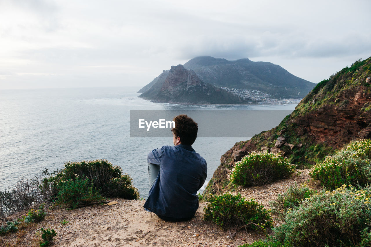 Man looking at mountains by sea against sky