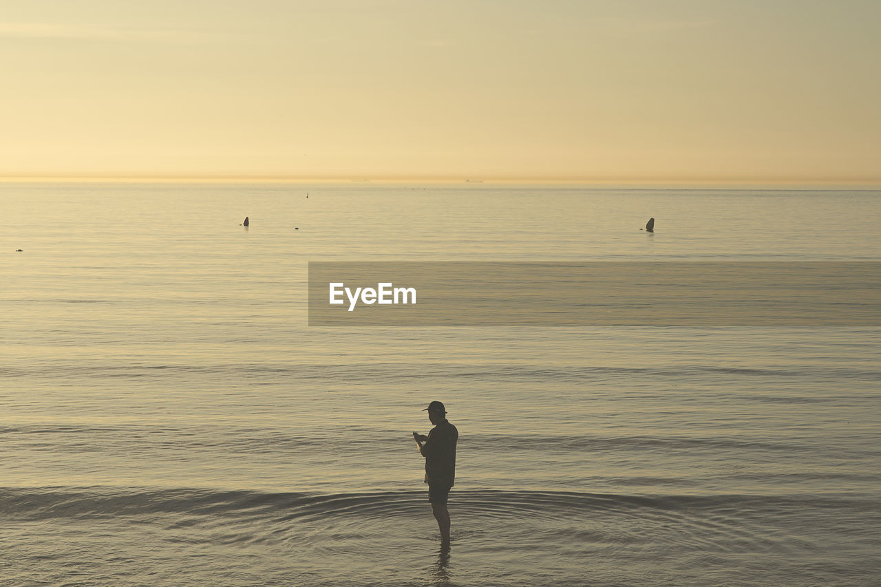 MAN STANDING ON SEA SHORE AGAINST SKY