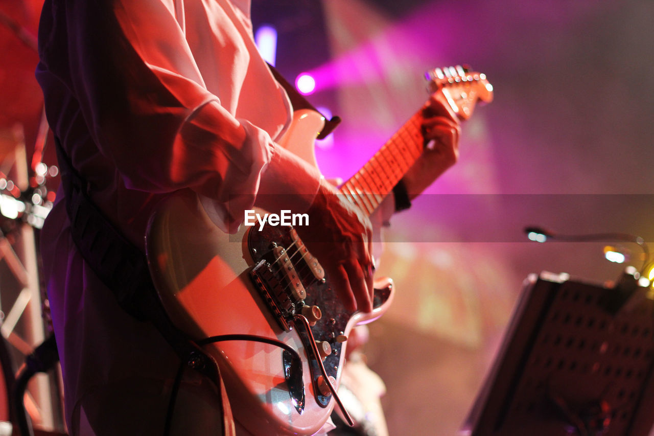 Midsection of man playing guitar in music concert