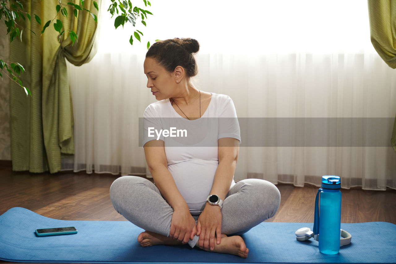 side view of young woman sitting on floor at home