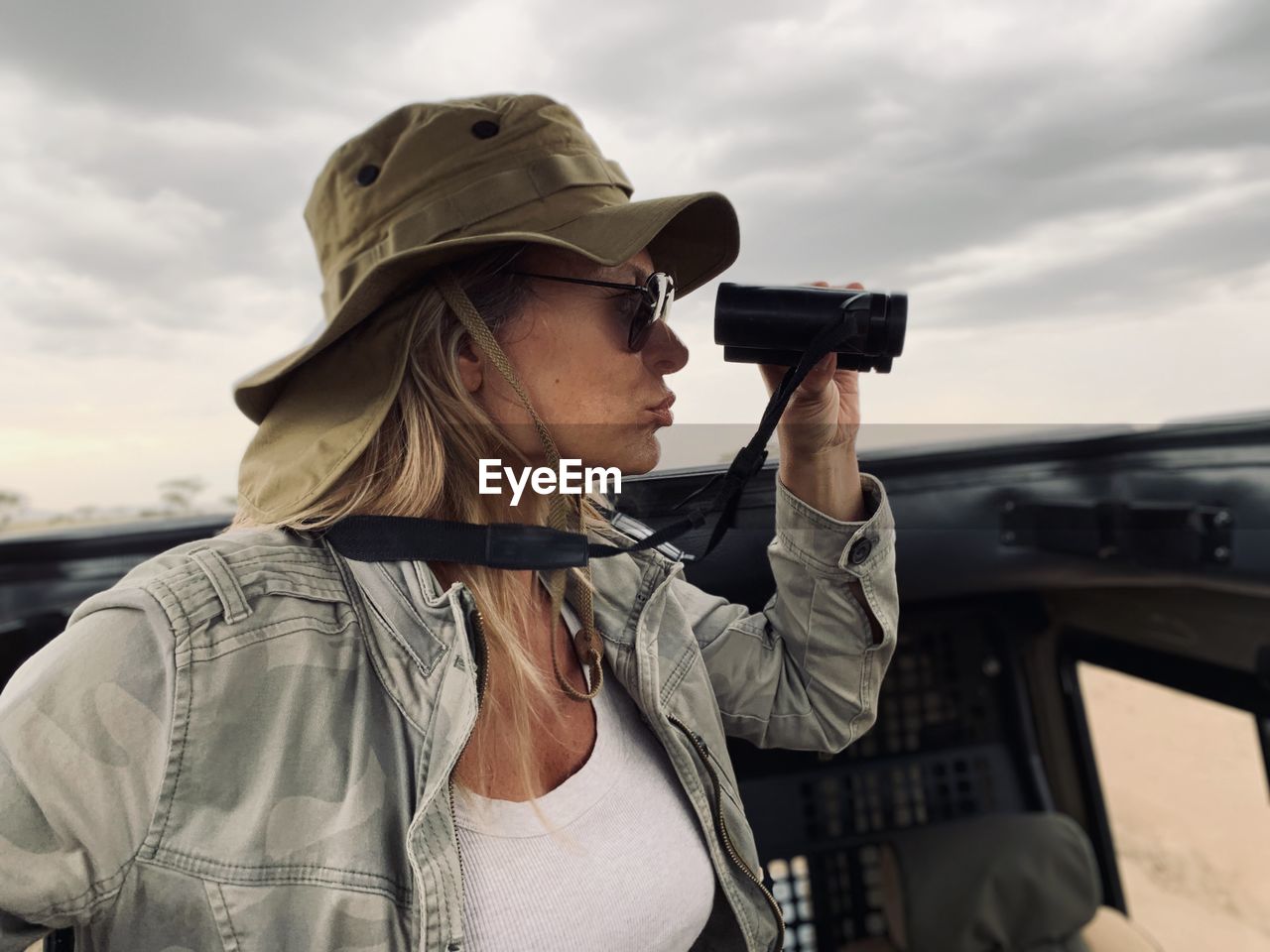 Woman looking through binoculars while sitting in safari vehicle at national park