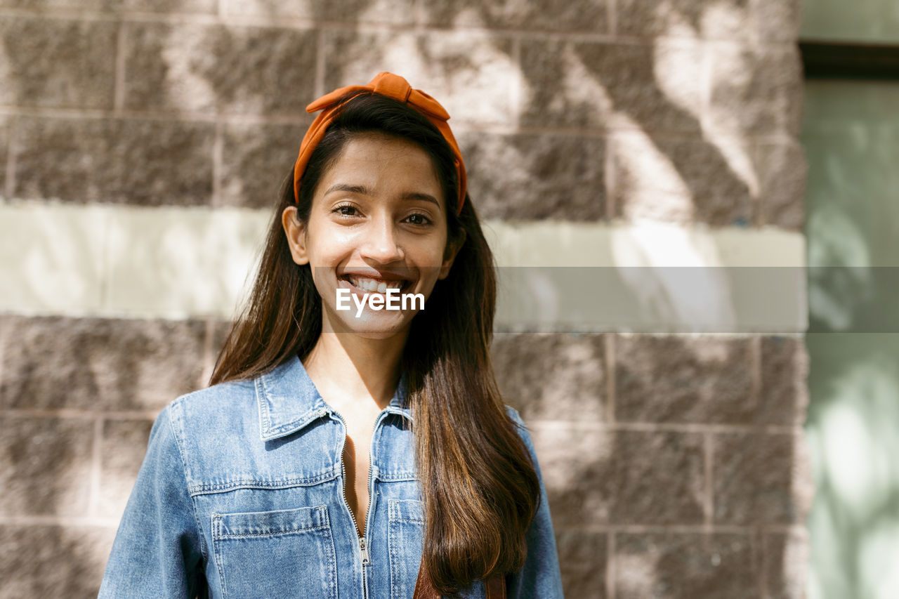 Young woman smiling while standing against wall