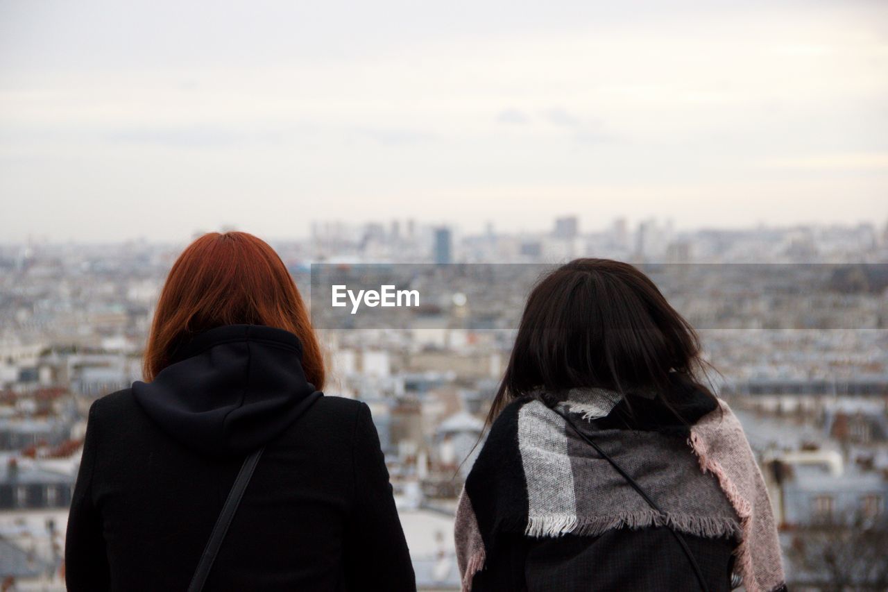 Rear view of women looking at cityscape against sky