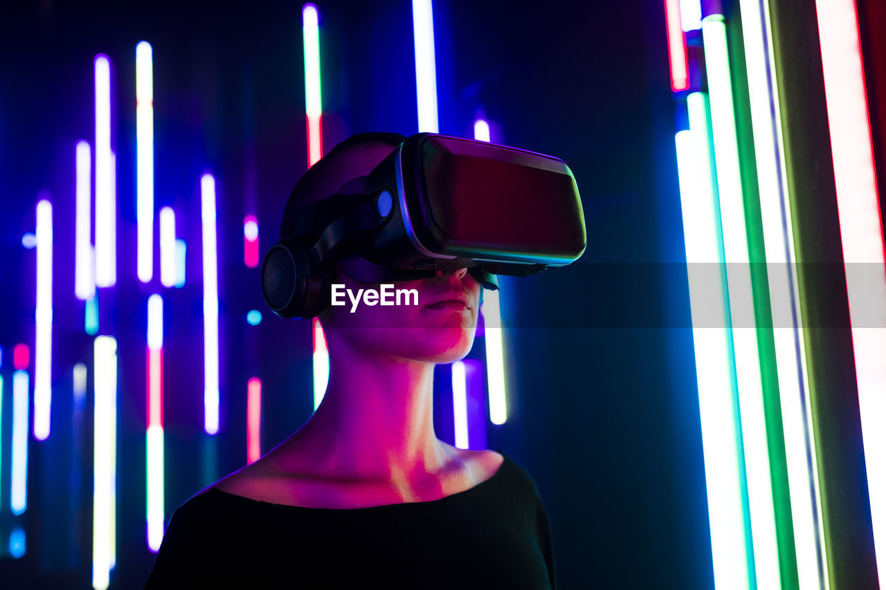 Woman wearing virtual reality simulator near colorful illuminated lights