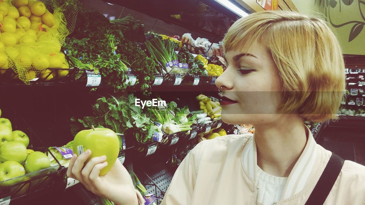 Close-up of blond woman looking at granny smith apple at supermarket