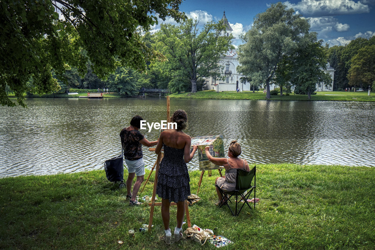 REAR VIEW OF PEOPLE ON LAKE BY TREES