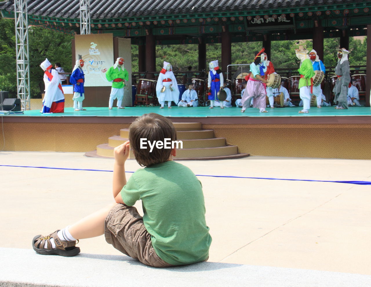 Rear view of boy looking at dance performance while sitting in city