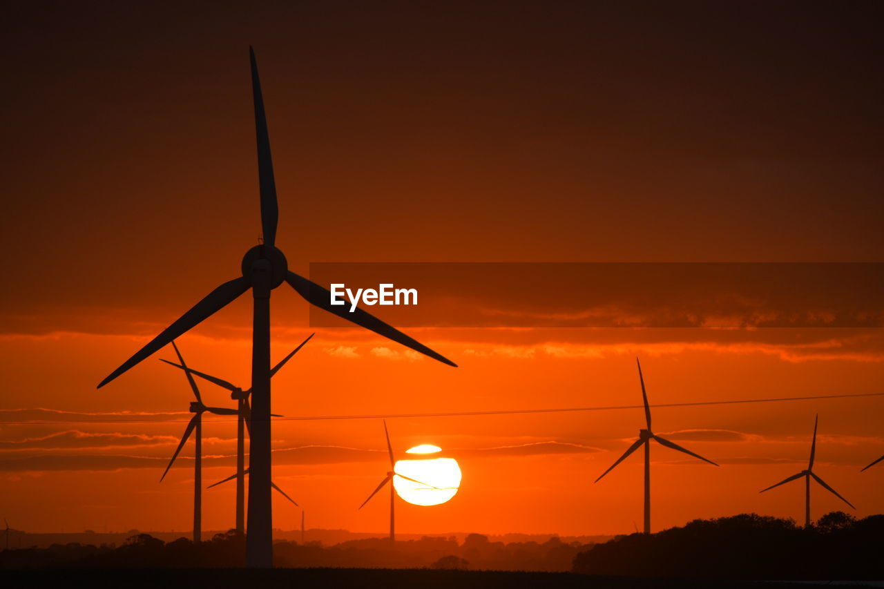 A bright red sunset through wind turbines