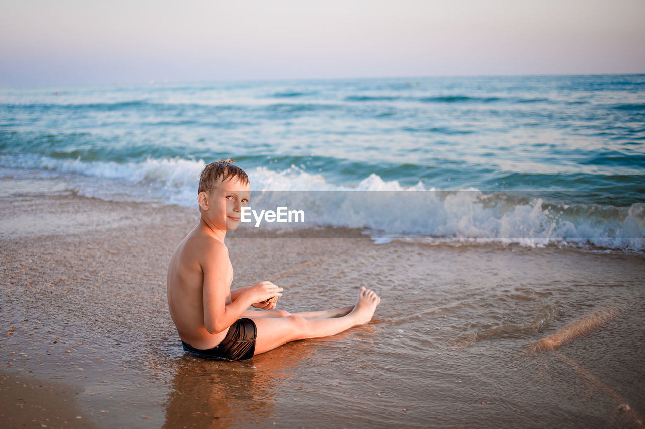 full length of shirtless boy playing at beach