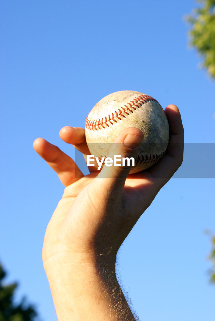 Low angle view of hand holding baseball against sky