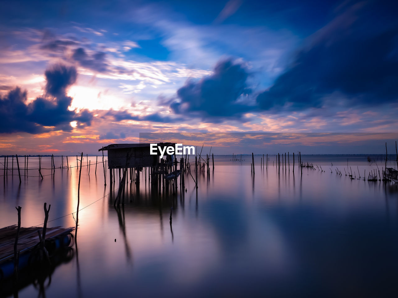 Wooden posts in lake against sky at sunset