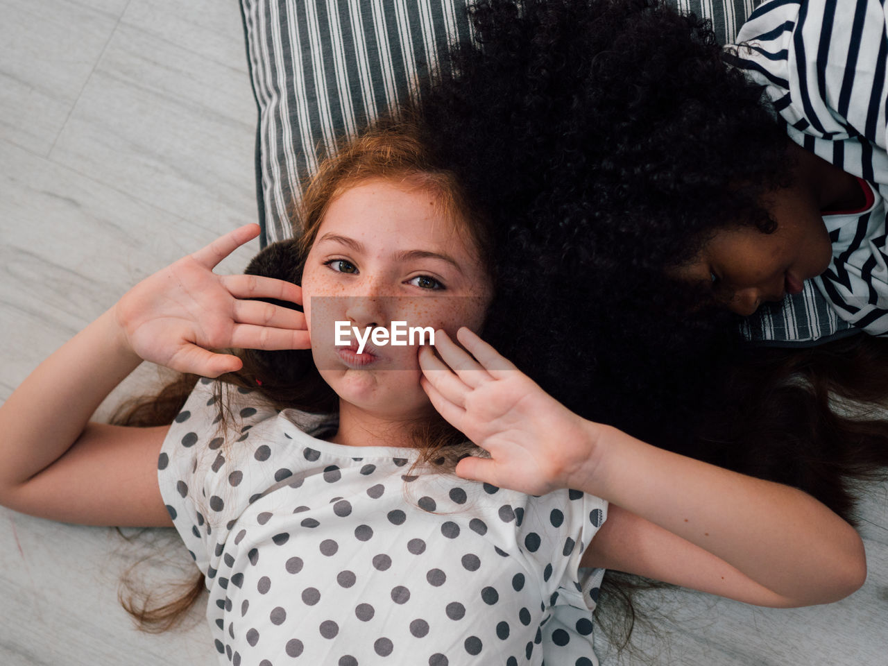 Portrait of girl with sister lying down on floor at home