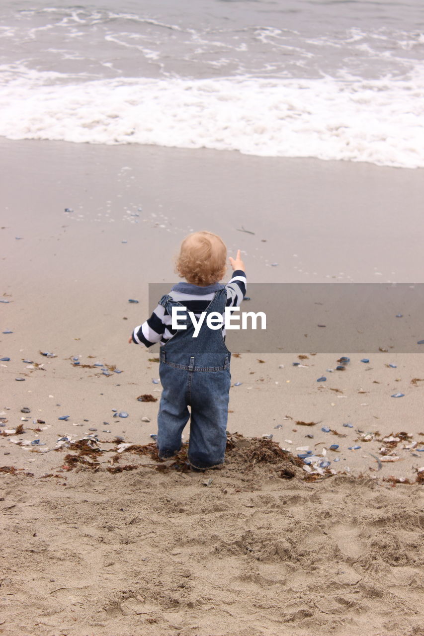 Rear view of boy standing on sand at beach