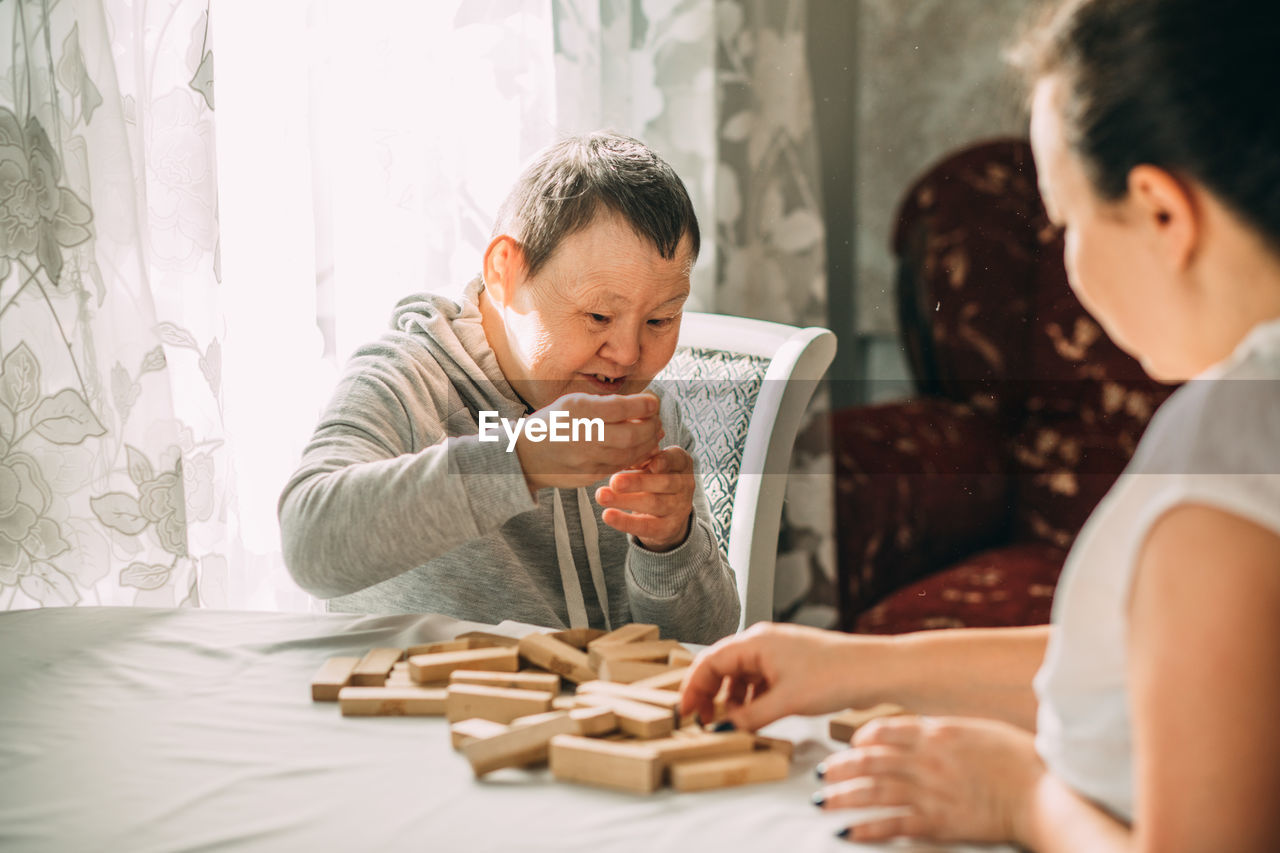 Elderly woman down syndrome builds tower of wooden cubes, development of cognitive fine motor skills