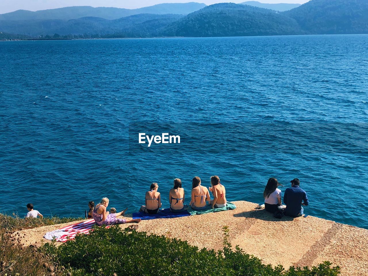 Rear view of people sitting on pier at sea